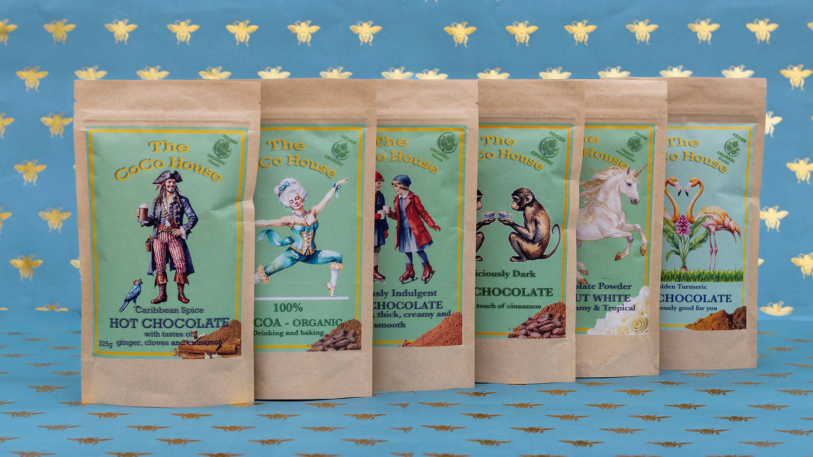 six packages of hot chocolate with colourful labels on a blue background with gold bee pattern